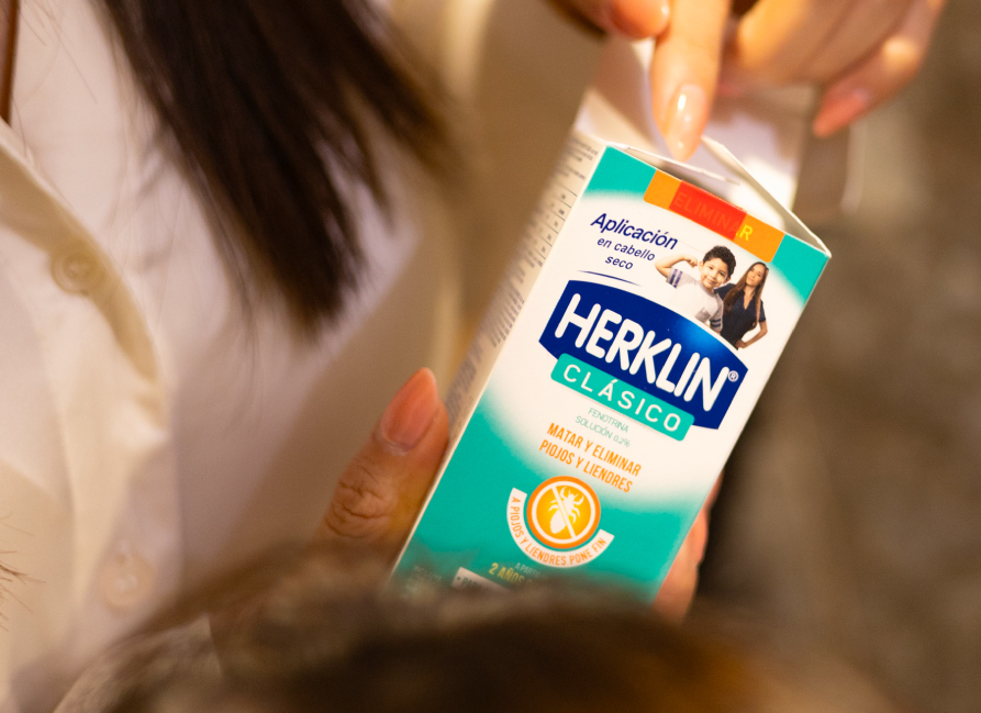 Una mano sostiene la caja de Herklin Clásico junto al cabello.