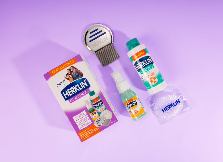Kit Herklin 3 en 1: empaque, peine lendrera, spray y gorra sobre fondo lila.